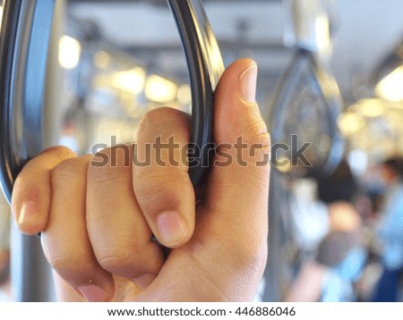 A hand holding handrails in a public transit train or subway or metro, stood among many people that will go to work in the morning