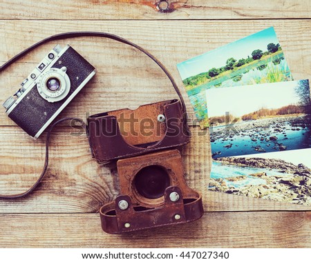 Vintage, very old film camera and fotos on brown wooden background. Photo with retro filter effect.