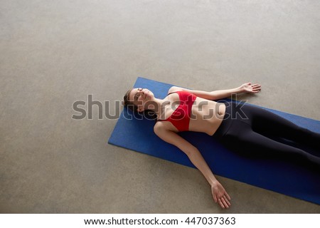 Top view portrait of a young woman resting in shavasana on the yoga mat at gym Royalty-Free Stock Photo #447037363