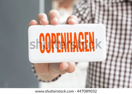 Man hand showing COPENHAGEN word phone with  blur business man wearing plaid shirt.