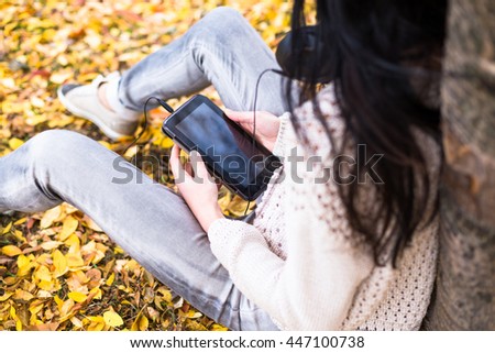 Young happy teenage girl using her tablet and listening to music in autumn city park. Fall life-style picture