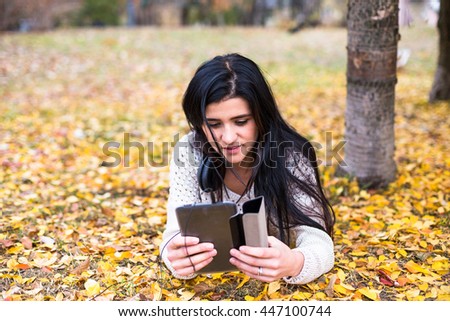 Young happy teenage girl using her tablet in autumn city park. Fall life-style picture