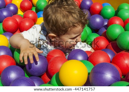 Baby boy having fun playing in a colorful plastic ball pool in a playground