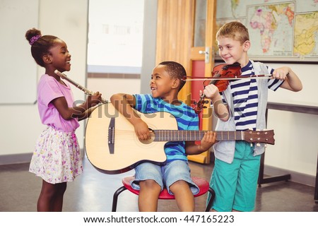 Smiling kids playing guitar, violin, flute in classroom at school Royalty-Free Stock Photo #447165223