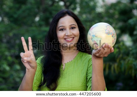 Young woman holding globe and making victory gesture