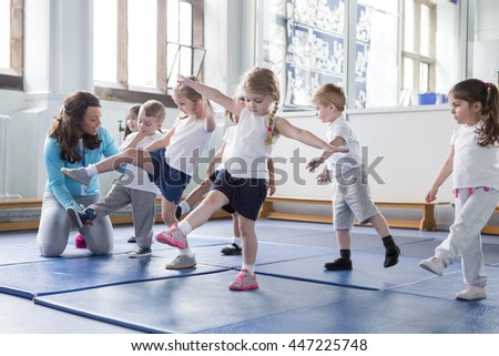 Nursery teacher helping one of her students during a physical education lesson. Royalty-Free Stock Photo #447225748