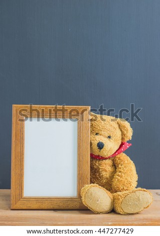 Photo frame with single brown teddy bear sitting on old wooden table, black background. Emphasizing copy space for write text.