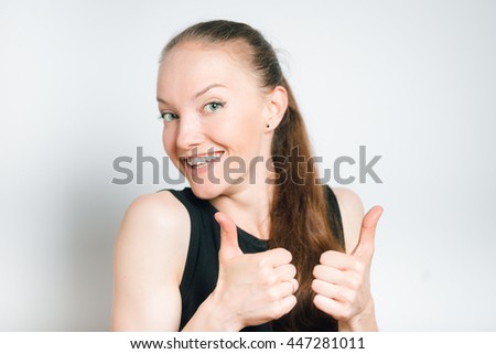 beautiful young woman showing thumbs up, isolated on a gray background