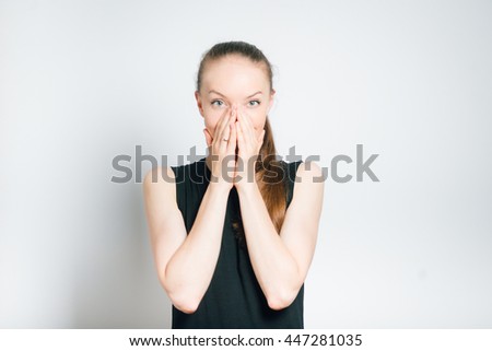beautiful young woman in shock closing mouth with hands, isolated on a gray background