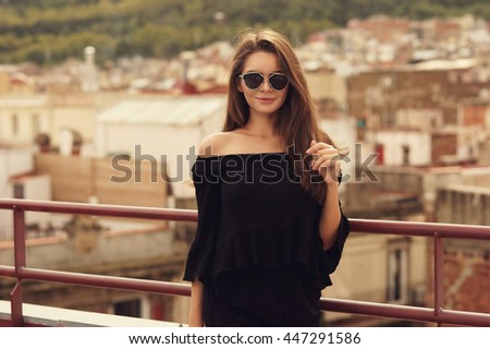 Young beautiful woman in black dress and leather jacket standing at roof near fence