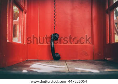 black handset hanging in a red telephone box. telephone receiver hanging touching the floor in a red call telephone booth. the concept of technological progress and the development of communication Royalty-Free Stock Photo #447325054