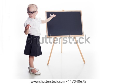 Little girls standing in front of blackboard and show on it with hand. White background. Concept: show or draw graph. Royalty-Free Stock Photo #447340675