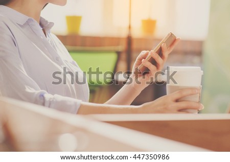 Phone usage. Cropped picture of hands of businesswoman using her smartphone and holding a cup of coffee