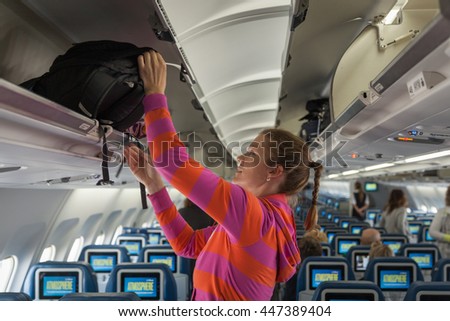The young girl placed her hand luggage into the compartment on the plane Royalty-Free Stock Photo #447389404