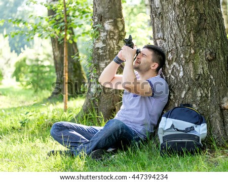 Portrait of young hipster man with camera outdoors. Young male photographer photographing nature on summer day.