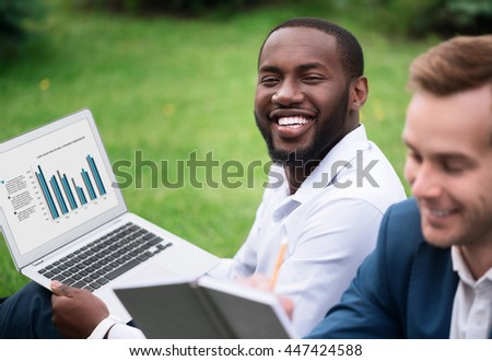 Positive man sitting on the grass with his colleague