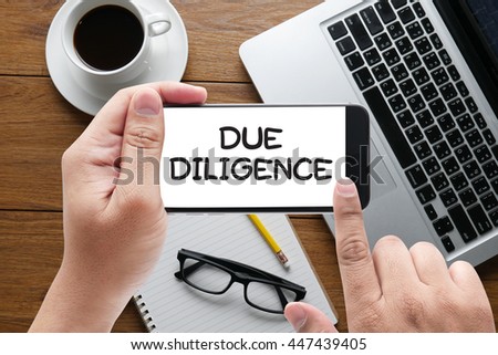 due diligence  message on hand holding to touch a phone, top view, table computer coffee and book