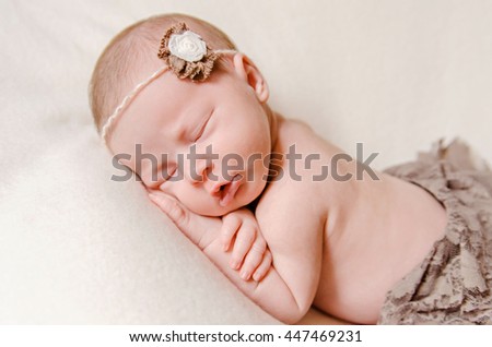 Close-up beautiful sleeping baby girl. Newborn baby girl, asleep on a blanket. A portrait of a beautiful, seven day old, newborn baby girl wearing a large, fabric headband with a flower. Closeup photo