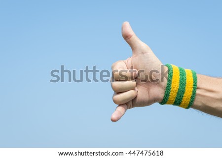 Athlete hand with yellow and green Brazil colors wristband giving a classic shaka surfer sign against blue sky