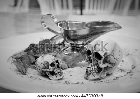 skull on the white dish ,knife and stainless Sauce Boat with bone and Steak on the table at restaurant. skull steak.  black and white photography / Still life style