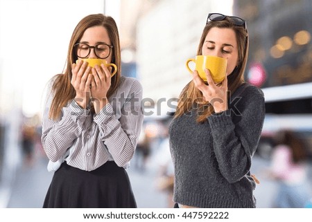 Twin sisters holding a cup of coffee on unfocused background