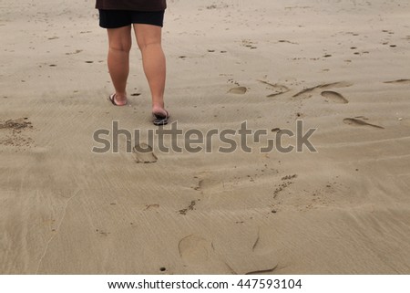 Woman walking on the beach towards the sea and  see footprint. Take photo the legs only. 