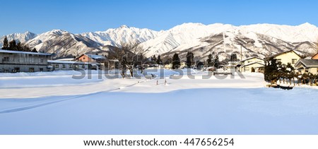 Panoramic alpine landscape of snow covered village and mountains on Honshu, Japan.  Villagers farm on the flat land at the base of the mountain range in the warmer months of the year.