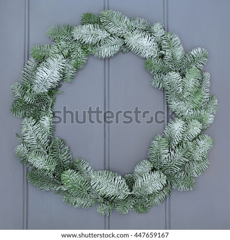 Christmas blue spruce fir wreath with snow on grey front door background.