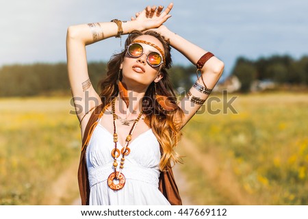Pretty amazing free red-haired hippie girl dancing outdoors, feathers and braids in her hair, white dress, vest with fringe, accessories, sunglasses, tattoo flash, indie, Bohemian, bo-ho style Royalty-Free Stock Photo #447669112
