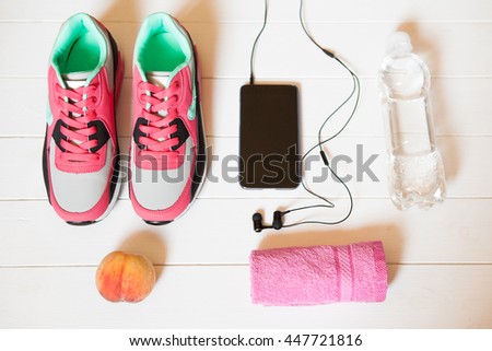 Red sneakers with towel, peach, bottle with water, smartphone with headphones on white wooden background indoors. Sports and fitness background, healthy lifestyle concept.