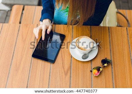 There are a cop of coffee, sunglasses and tablet on the table. This picture shows the girl working on the tablet.
