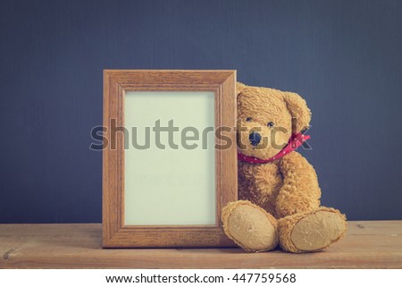 Photo old wood frame with single brown teddy bear sitting on old wooden table, black background. Emphasizing copy space for write text. image style vintage.