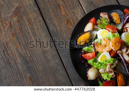 Seafood salad plate on wood half image copyspace. Portion of salad with grilled shrimps, mussels and octopus on side of picture on wooden background with free space