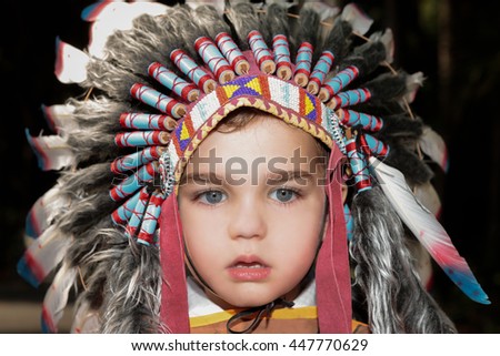 a close up of a boy with indian chief headpiece with blue eyes, background view is black.