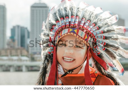 little boy wearing indian chief headpiece with multi colours looking into the lens,background view is blur.
