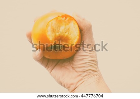 Hand holding ripe persimmon with bite mark. Photo with vintage filter effect.