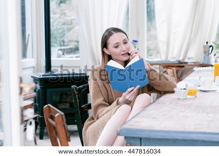 Woman sitting at dining table eating blackberries reading book