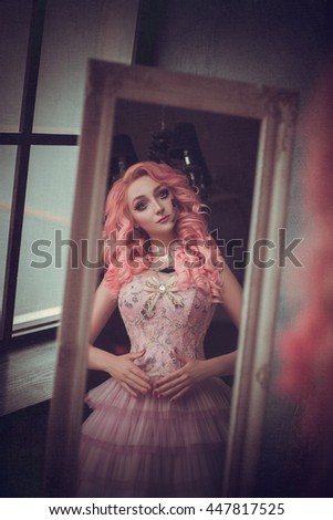 Unnecessary, forgotten, abandoned, children's doll. A woman with make-up cracks in her face looks at herself in surprise in the mirror. Pink hair, short dress. The old room. Creative colors