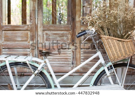 Bicycle with a basket of a dried bouquet flower stand in front of wooden and rustic house background. 