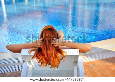 The young red-haired woman lying on a lounger near the swimming pool