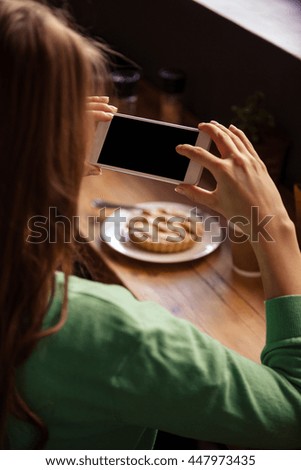 Over the shoulder view of hipster woman taking picture of pastry at cafe