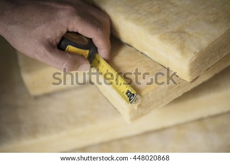 Hand measuring a fiberglass batt. Image of home insulation. Royalty-Free Stock Photo #448020868