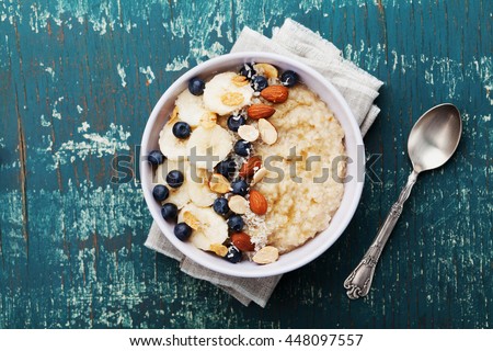 Bowl of oatmeal porridge with banana, blueberries, almonds, coconut and caramel sauce on teal rustic table, hot and healthy food for Breakfast, top view, flat lay Royalty-Free Stock Photo #448097557