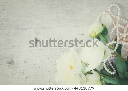 White fresh peony flowers with pearls jewellery on aged white wooden table with copy space, retro toned