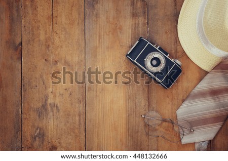Vintage camera, glasses and fedora hat on wooden background. Top view
