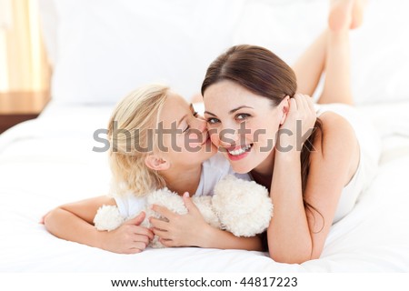Cute little girl kissing her mother lying on a bed