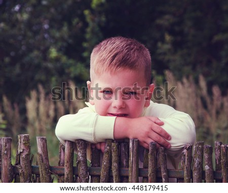 Sad little boy looking at something against blurred natural background.