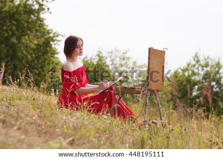 the young woman in a red dress draws outdoors