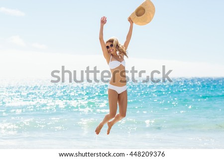 Carefree young woman holding hat and jumping on beach