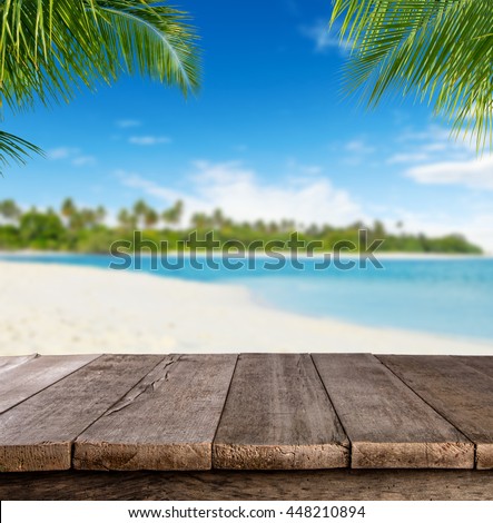 Empty wooden planks with blur beach on background, can be used for product placement, palm leaves on foreground